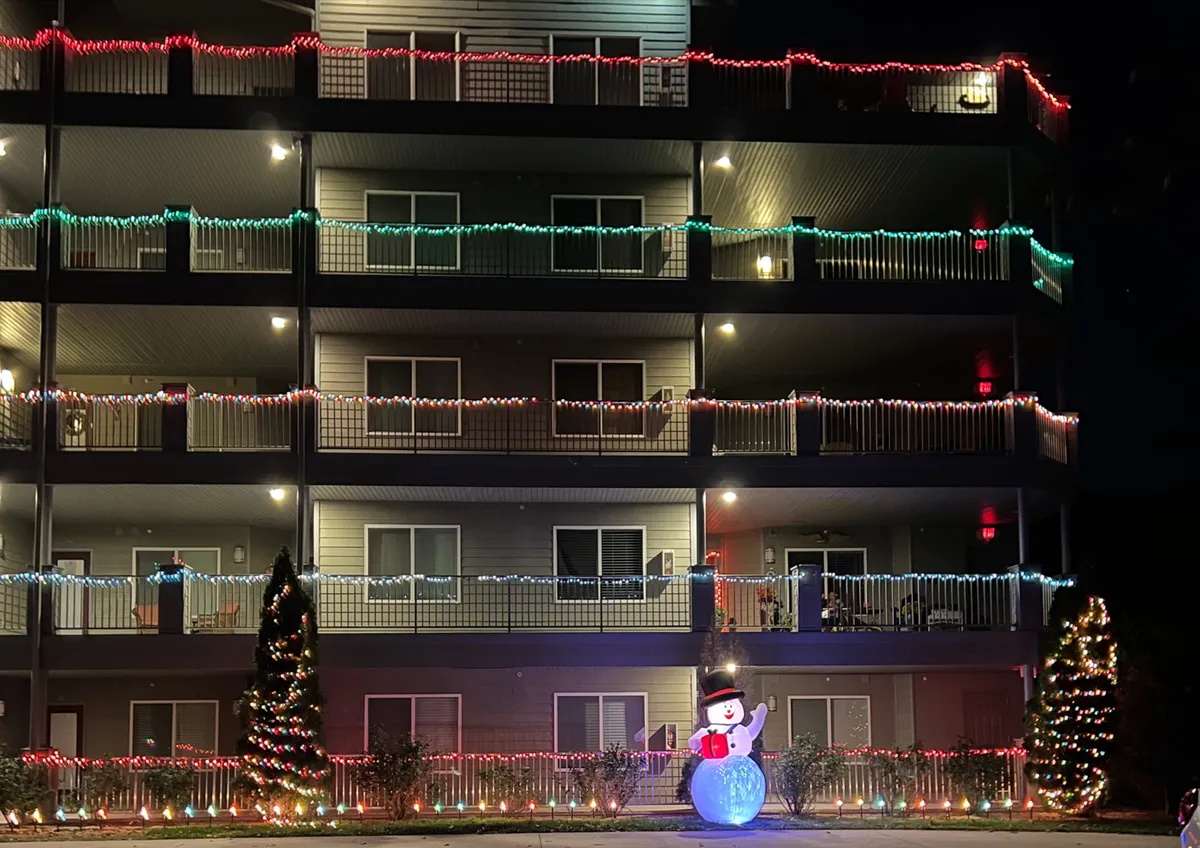 An exterior shot of the property featuring festive Christmas lights on balconies, a decorated tree, and a snowman in the foreground. The scene is cheerful and inviting, suggesting a lively, communal atmosphere ideal for group gatherings and memory-making.