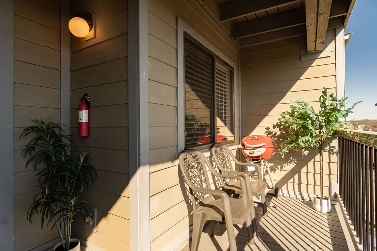 An exterior shot of a private deck outfitted with two chairs, a small grill, and potted plants. The balcony overlooks a serene view, offering an inviting space for morning coffee or evening toasts.