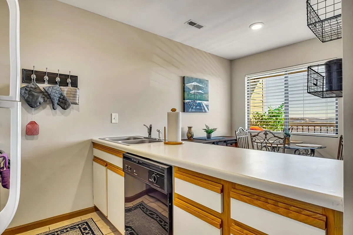 A view of the kitchen counter with a visible dishwasher, adjacent to a dining table with chairs and a window offering a pleasant view. The area is arranged for cooking, dining, and entertaining, radiating warmth and welcoming energy.