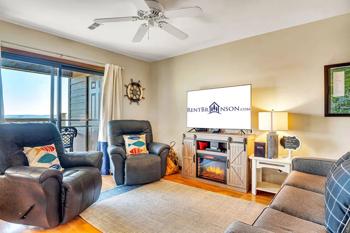 This cozy interior features comfortable recliners, an entertainment center with a TV, and abundant natural light from windows. The layout is ideal for socializing or unwinding after a day of exploration, and the hints of balcony and outside views subtly tie the interior to the surrounding area.