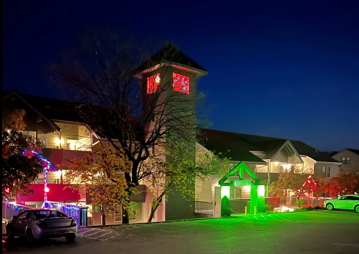 This exterior shot captures the property at dusk, with decorative lights illuminating the entrance and a green sign clearly marking the location. The tower with glowing windows adds charm and a sense of welcome, while the overall scene hints at the festive, social atmosphere guests can enjoy outdoors.