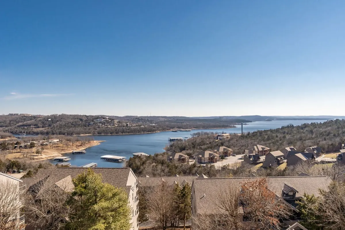 The image showcases a sweeping, top-of-the-hill panoramic view over a tranquil lake at sunset, with gentle hills and scattered homes dotting the shoreline. The scene is peaceful, with the vibrant sky reflecting off the water, inviting thoughts of relaxation and outdoor adventure.
