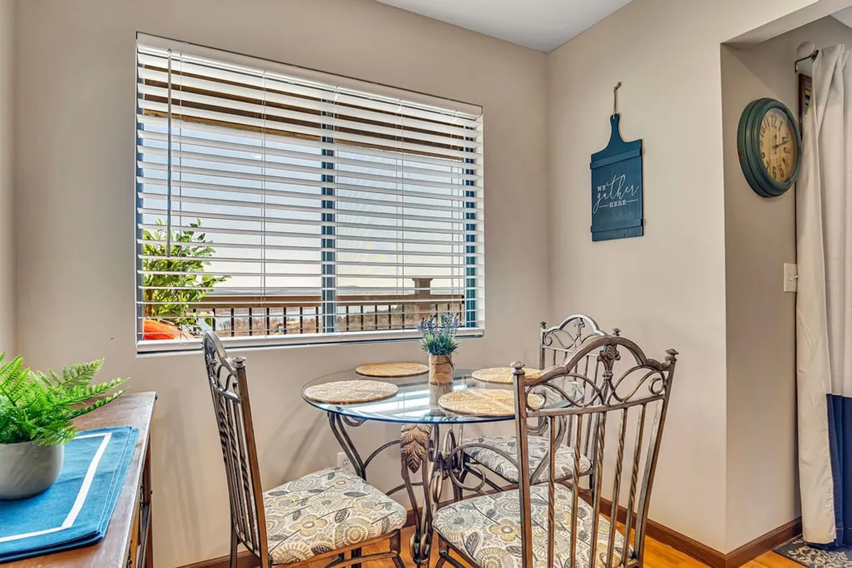 A cozy dining space with a circular table, slatted window blinds, a decorative wall clock, and a green plant. The setting is perfect for family meals, morning coffee, or celebratory dinners, exuding warmth and intimacy.