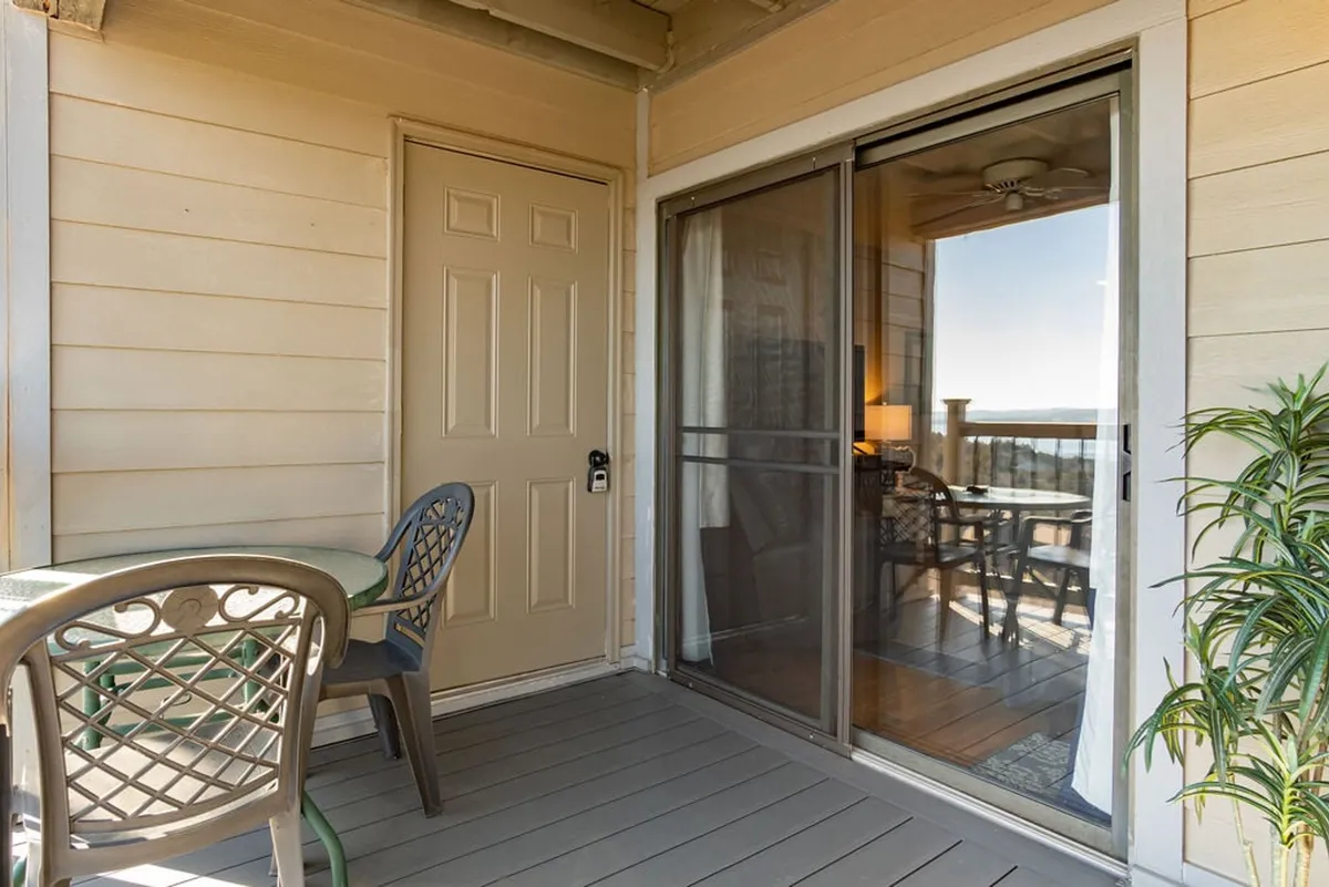 The view showcases a welcoming entryway and a comfortable outdoor seating area, framed by glass sliding doors. The space is ideal for relaxing, sipping morning coffee, or unwinding while taking in scenic views, hinting at connections to nature and the broader Ozarks setting.